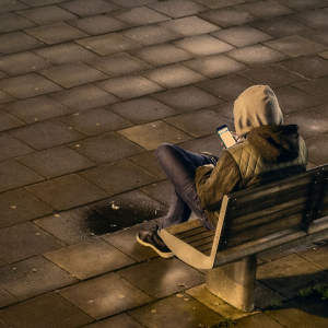 A teenager sat on a bench looking at their phone